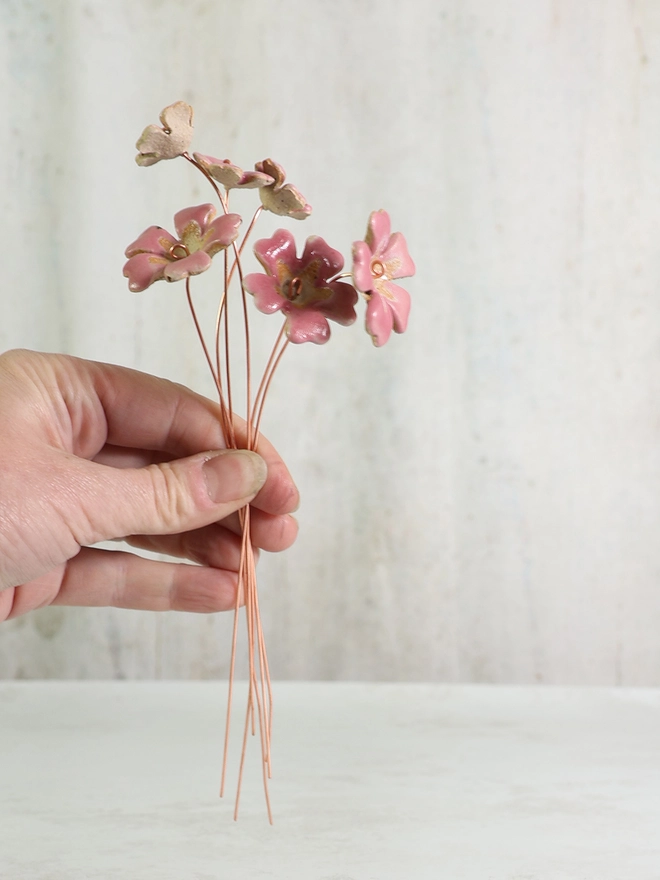 hand holds some ceramic primrose flowers on copper wire stems
