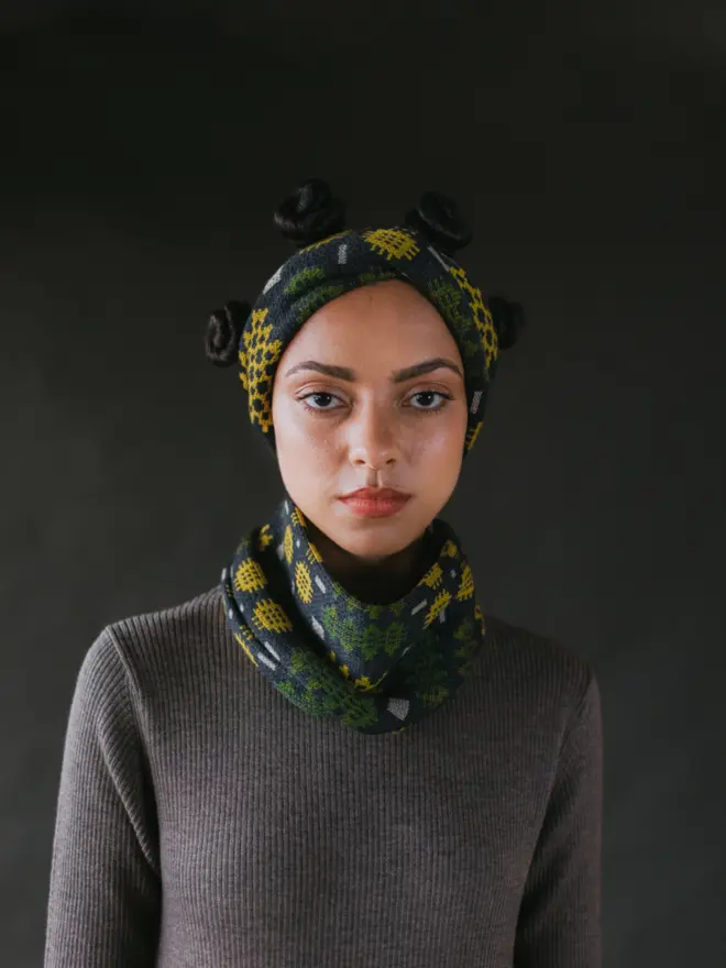 Model wearing pieces from MABLI's 'Carthen' collection, featuring the Carthen Wrap in the vibrant 'Anthracite/Pea' colour-way. The design showcases bold, colourful patterns inspired by traditional Welsh blanket tapestry.