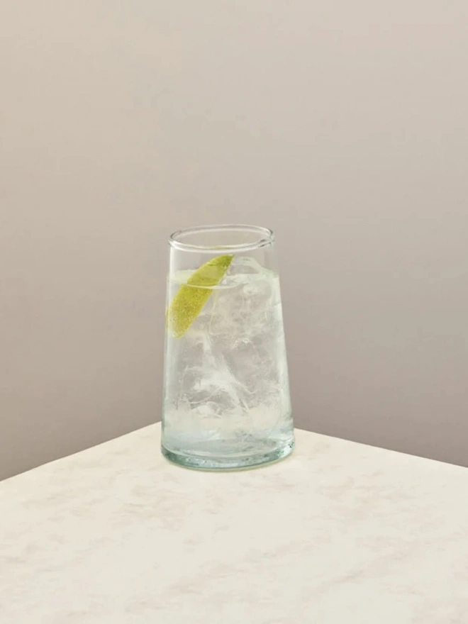 Highball Glasses (Set Of 1 Or 4), a highball glass sitting on a plain counter top against a white backdrop. It is filled with a soft drink. 