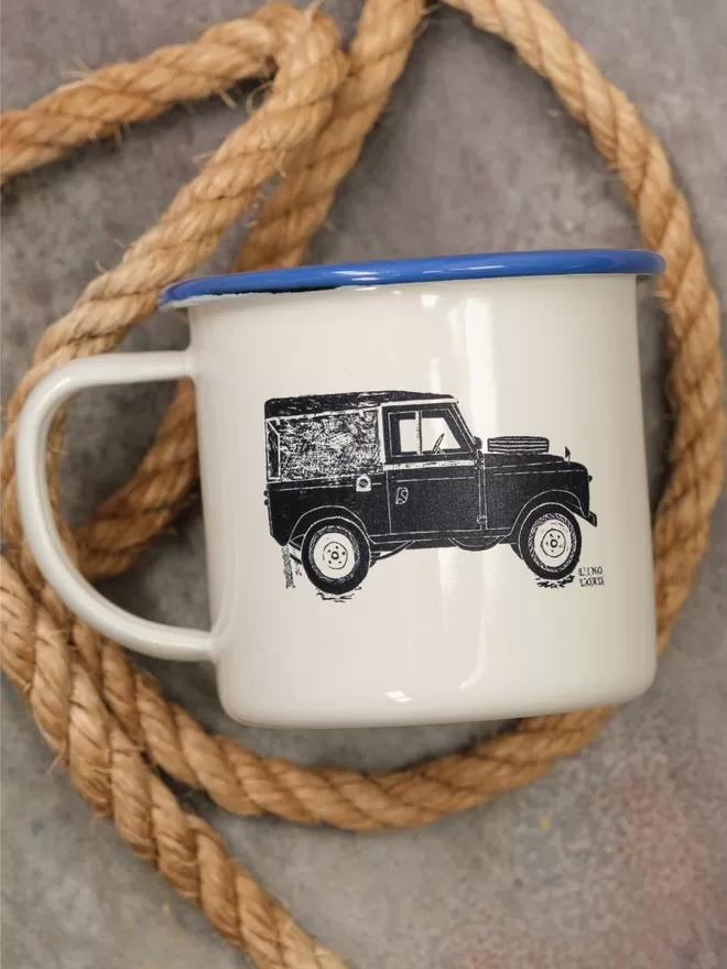 Picture of a Cream Enamel Mug with a Blue Rim with a Land Rover design etched onto it, taken from an original Lino Print