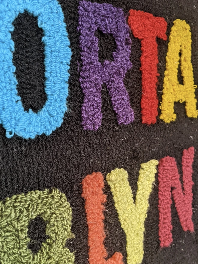 Letters O,R,T,A,L,Y,N in primary wool on black wool background