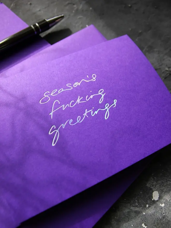 Hand foiled cash card or money wallet in a royal purple colour handfoiled in shiny holographic text which says 'season's fucking greetings'.