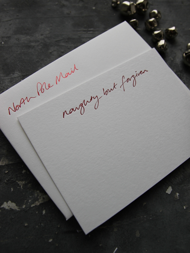 Christmas notecard from Santa that has a tick box for Naughty But Forgiven in red foil with an envelope that says North Pole Mail