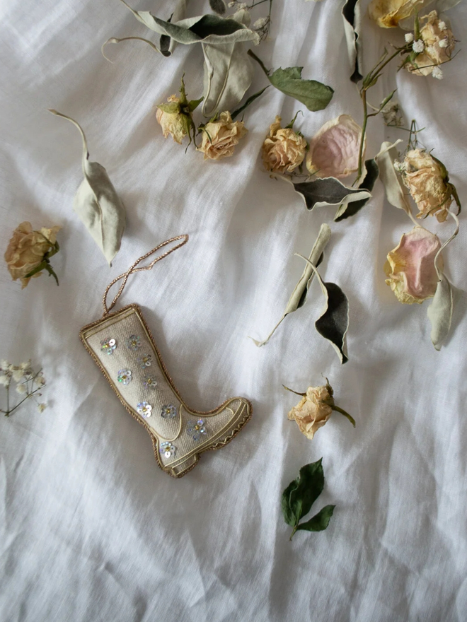 embroidered linen wellington boot decoration. wellington boot-shaped embroidered decoration placed on white sheet background with dried flowers