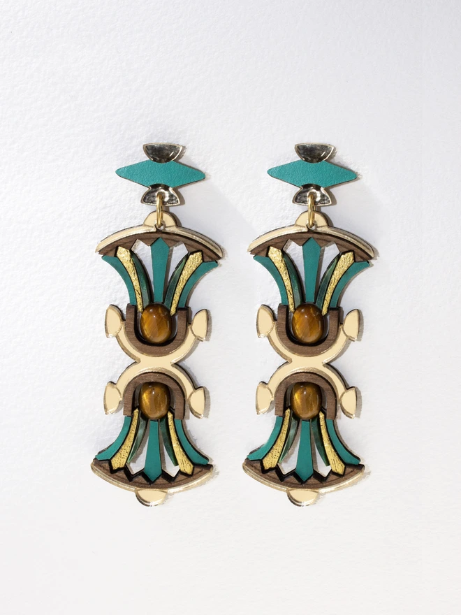 A gold and green pair of earrings on a blurred background