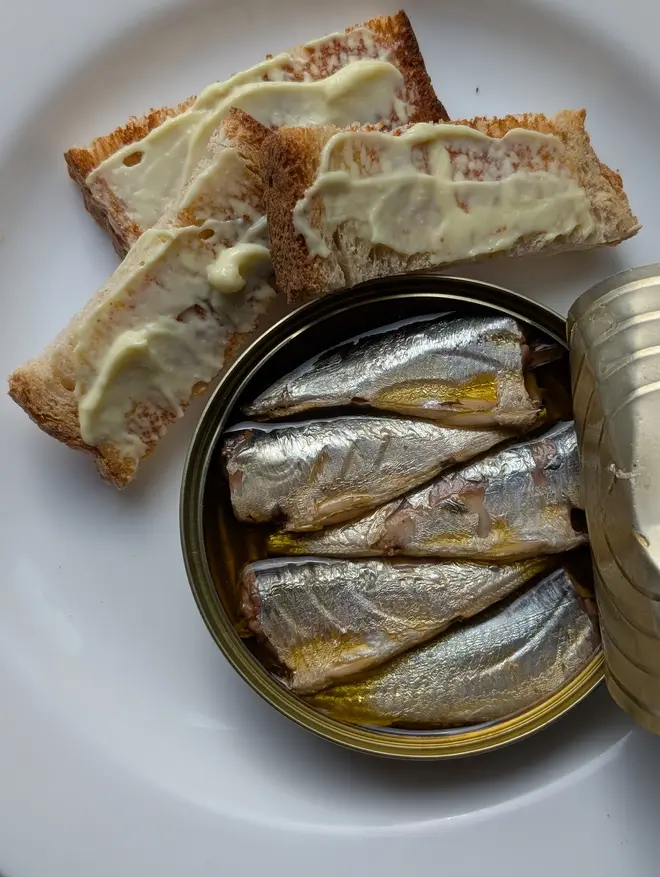 An open tin of Sea Sisters Cornish Sardines with Chill Extra Virgin Olive Oil on a white plate alongside some buttered bread