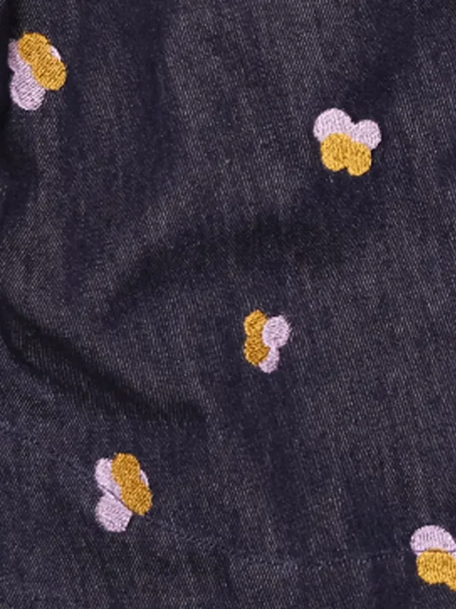 Close-up of Studio Koter's Denim Petal fabric, dark cotton denim with lilac and gold embroidered petals.