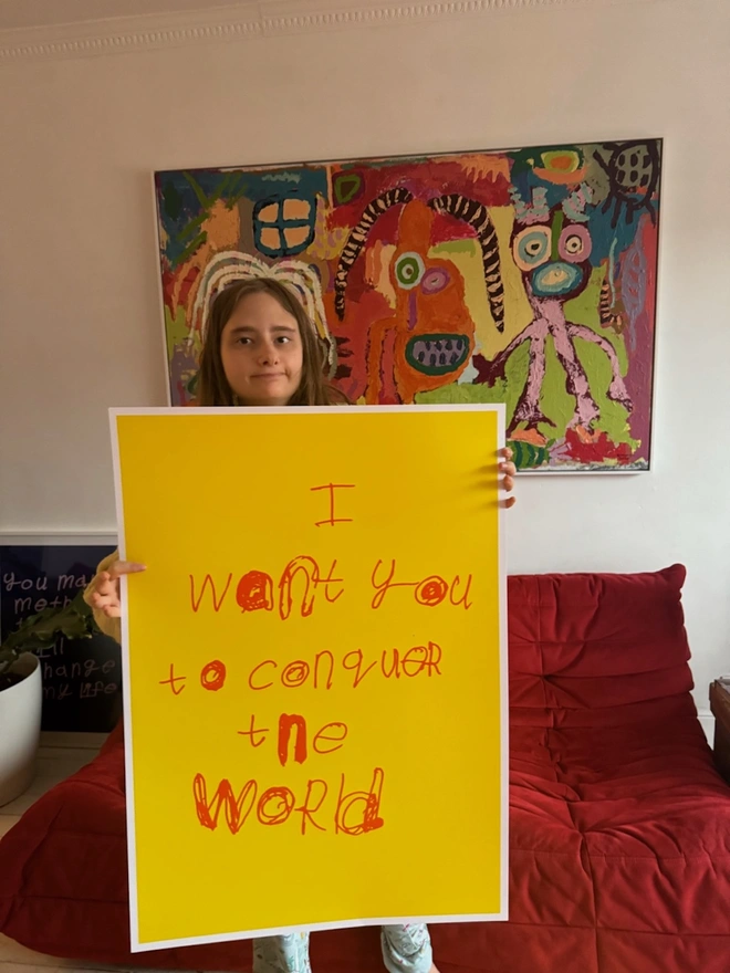 Piper is holding up her large screen print that its bright yellow with pipers unique orange font