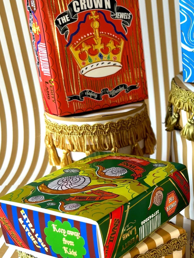 The Crown Jewels Matchbox, a red matchbox with a crown design sitting on a decorated surface accompanied by other accessories. 