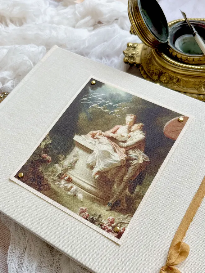 Luxury fabric printed wedding guest book featuring an images of lovers from an 18th century rococo work of art. Linen covered book finished with ribbon