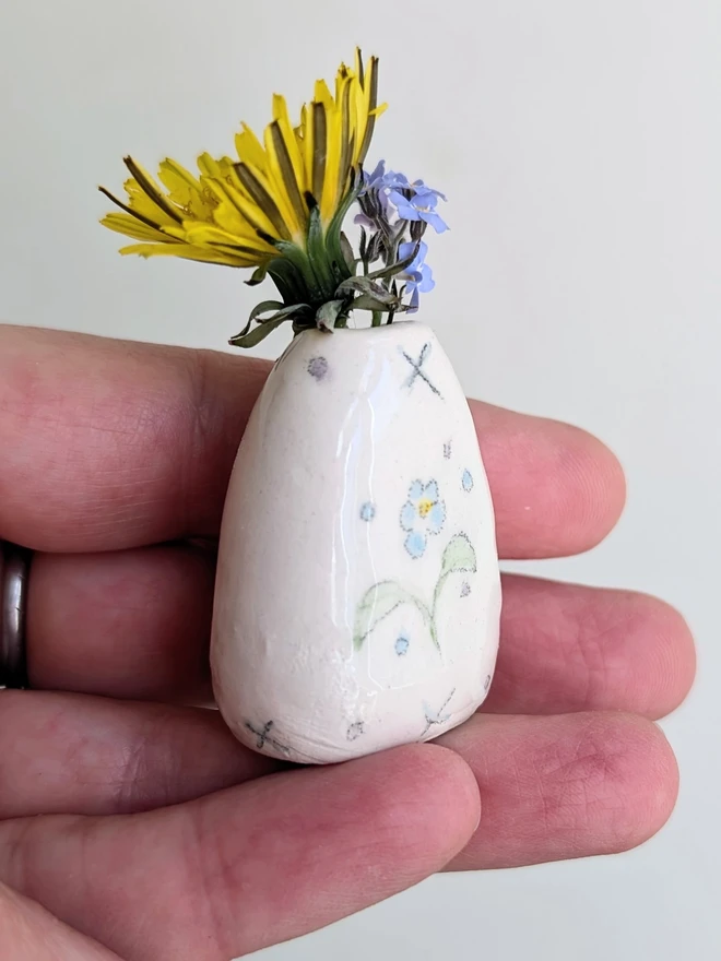 forget me not miniature vase held in a hand with dandelion and forget me not flowers in and hand painted illustration