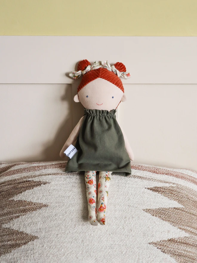 Handmade linen doll with light skin wearing dark green cotton dress and cream floral bows and tights. It has braided red hair made with corduroy.