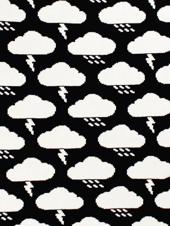 Detail of the reverse repeat pattern of white storm and rain clouds upon a black knitted background.