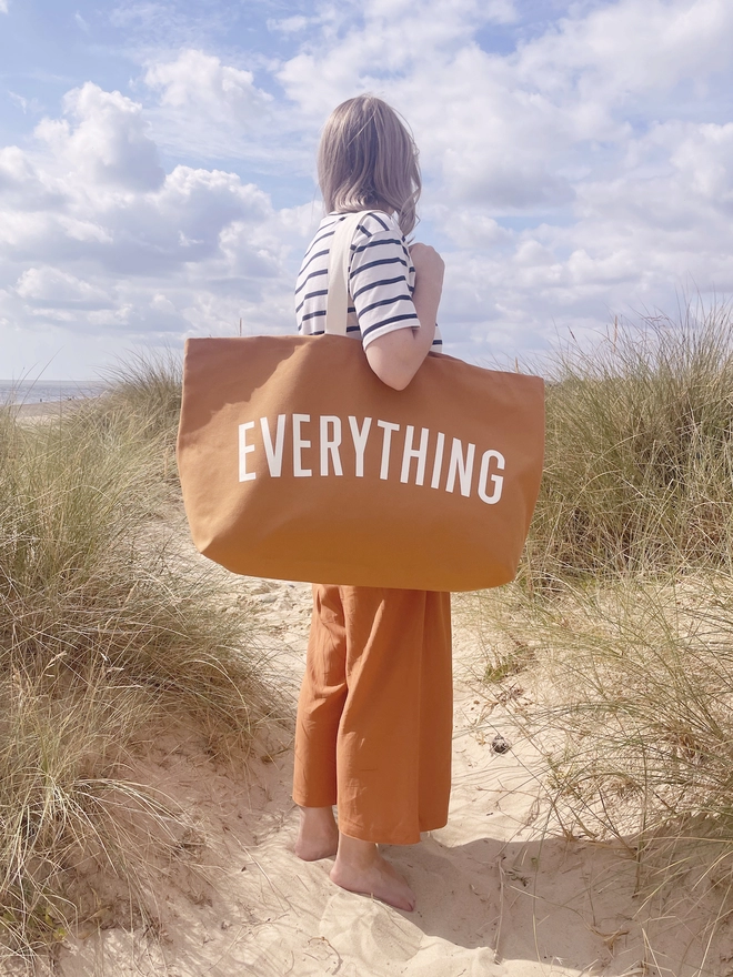 Model holding the Everything oversized tote bag in tan at the beach