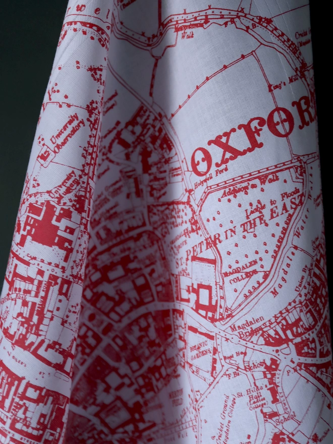 A Mr.PS Oxford map hankie printed in red held aloft in front of a dark wall.