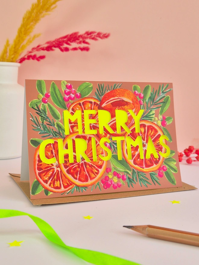 Christmas Card with blood oranges illustration, paper cut text that says Merry Christmas and a neon yellow backing paper 