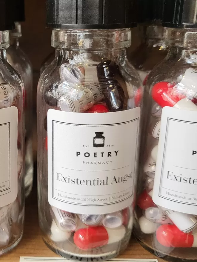 A row of glass bottles containing red and white Existential Angst poetry pills