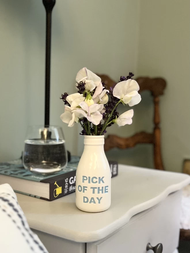 A handmade ‘pick of the day’ bottle/vase is filled with sweet peas sits on a bed side table.
