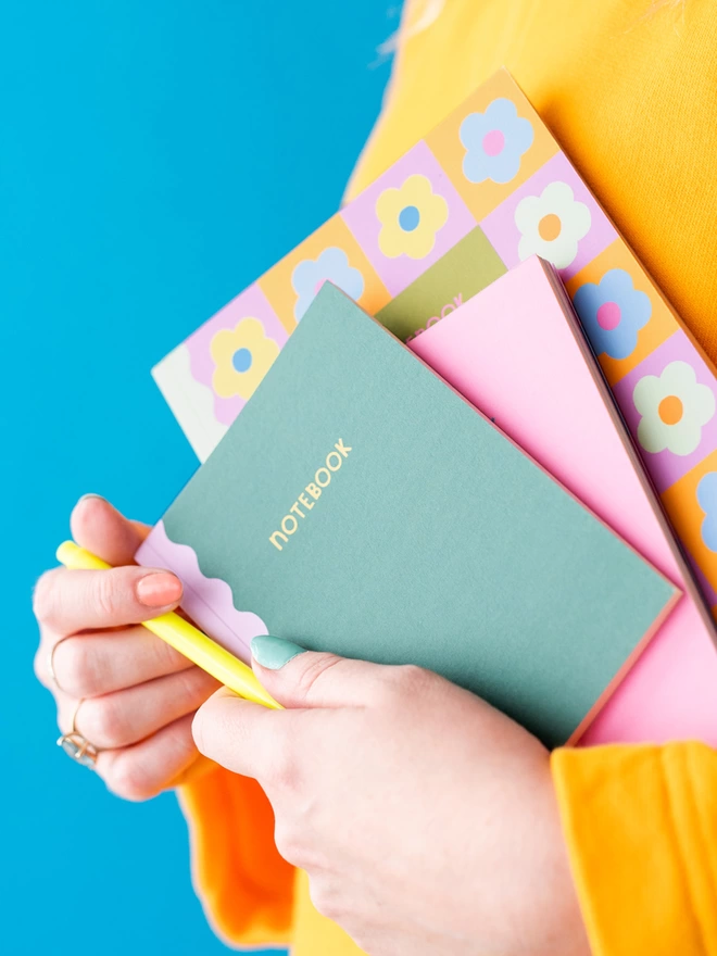 Holding a trio of notebooks from within the Happiness collection