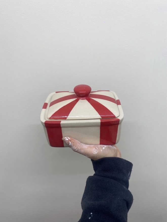 Circus Tent Stripes Handmade Ceramic Butter Dish, a red patterned butter dish held against a white backdrop. 