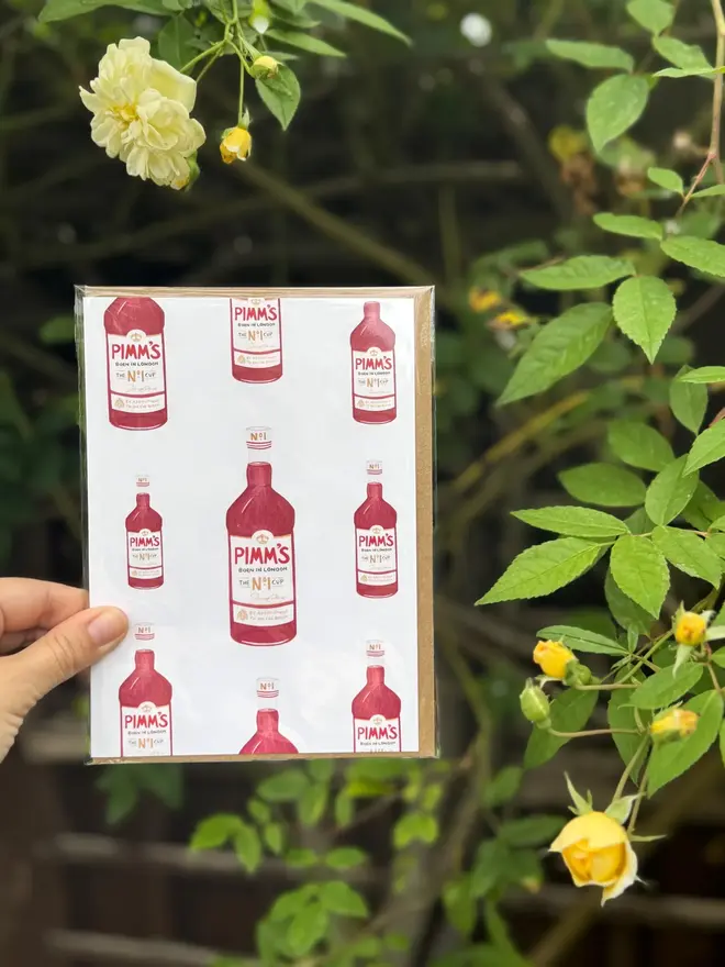 pimms bottle illustrated card. card photograped against leaves and flowers background.