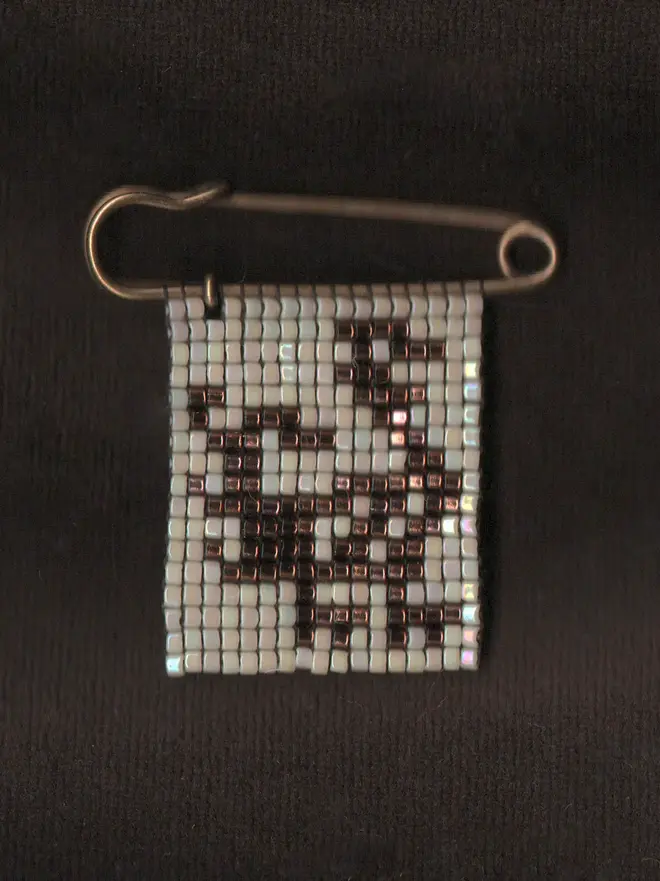 'creature iii' tiled beaded bird pin. a beaded pin badge with a brown bird on a pearl background.