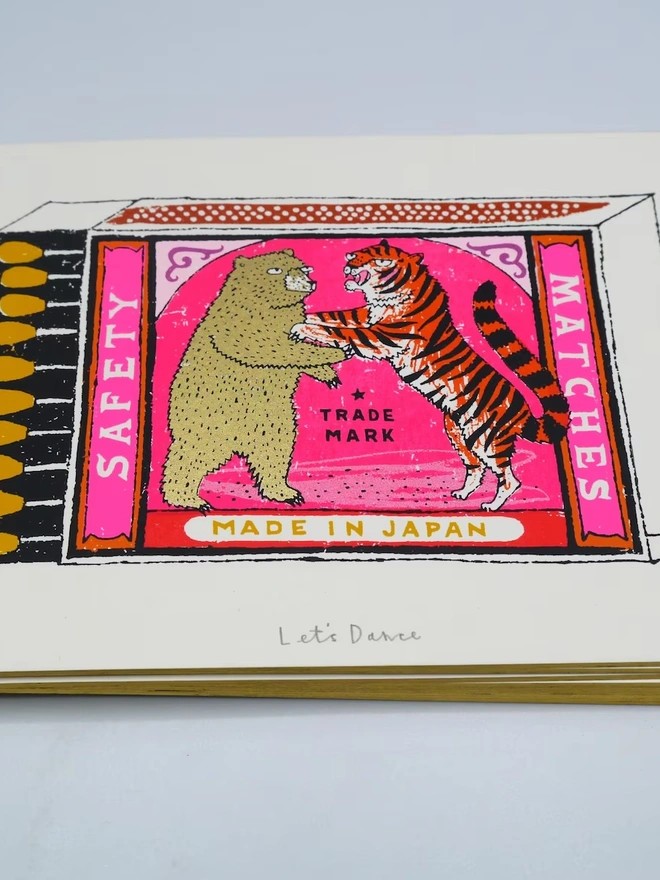 Bear And Tiger Matchbox Let's Dance, a colourful matchbox design on a white screenprint. It sits against a baby blue backdrop. 