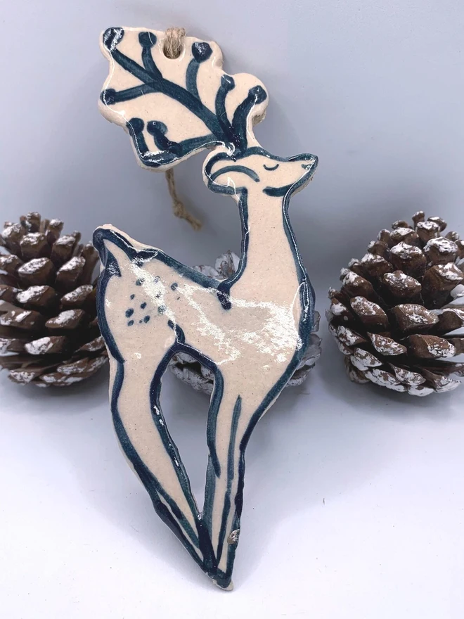 Handmade Ceramic Reindeer Ornament Scandinavian Folk Decor, a colourful reindeer decoration sitting on a plain surface joined by some acorns. 