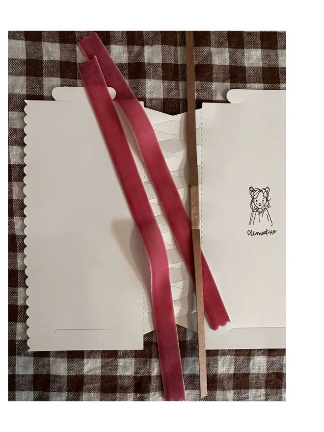 contents of cracker for make your own choice - white flat-laid cracker with bespoke cat illustration, velvet ribbon, and 'cracker snap' lying on white and brown gingham tablecloth
