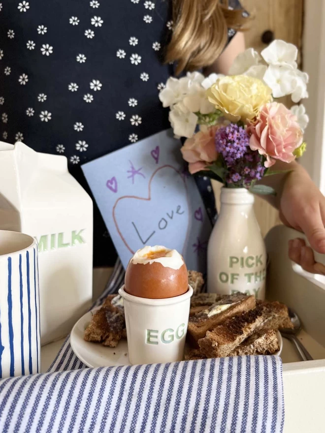 A Child has prepared a breakfast tray, using matching egg cup, milk carton and flowers bottle.