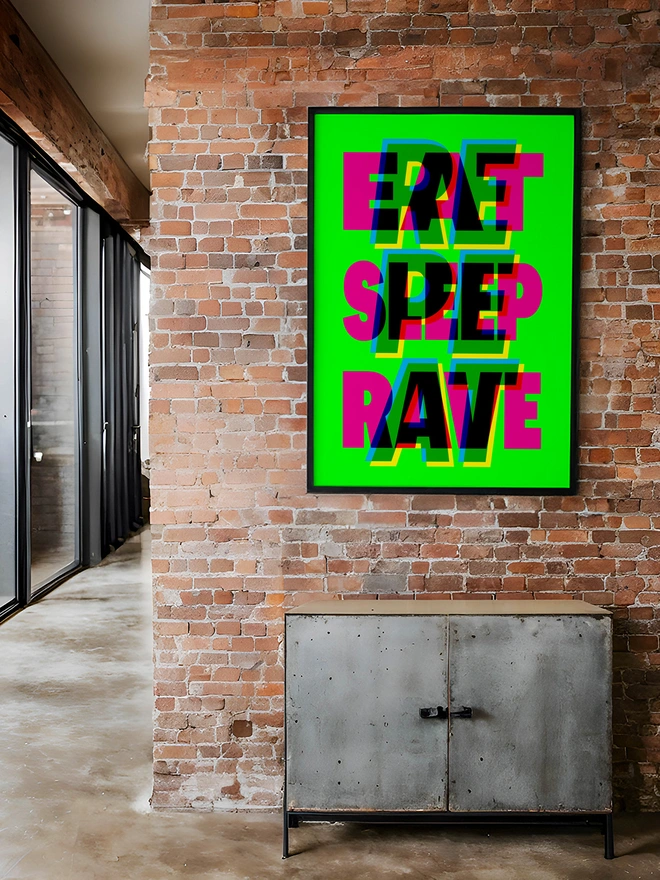 A colourful neon typographic giclée poster with the words "Eat Sleep Rave Repeat" hangs on a brick factory apartment. An ideal gift for an old raver!