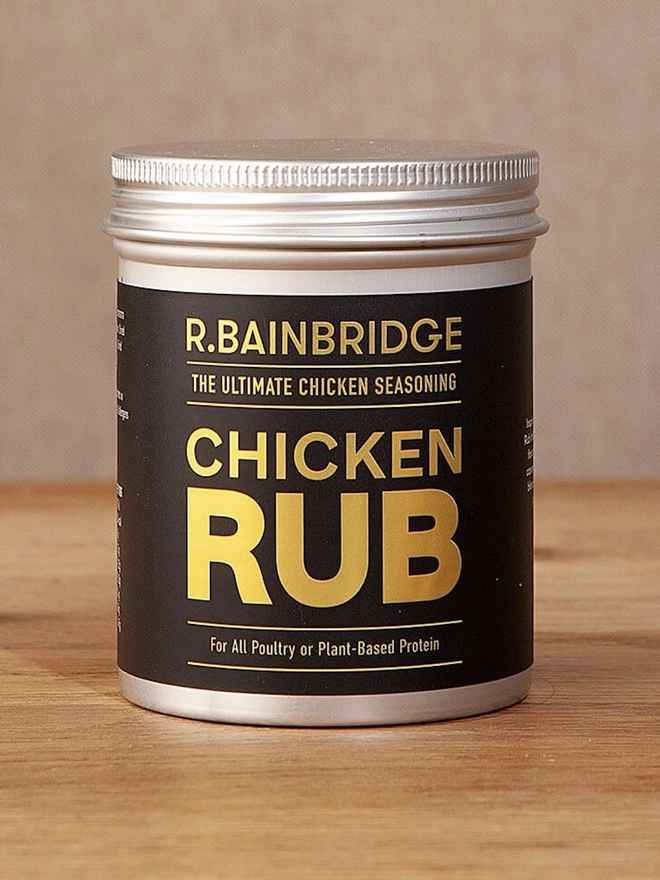 Chicken Rub Seasoning, a jar of seasoning on a wooden surface against a plain backdrop. 