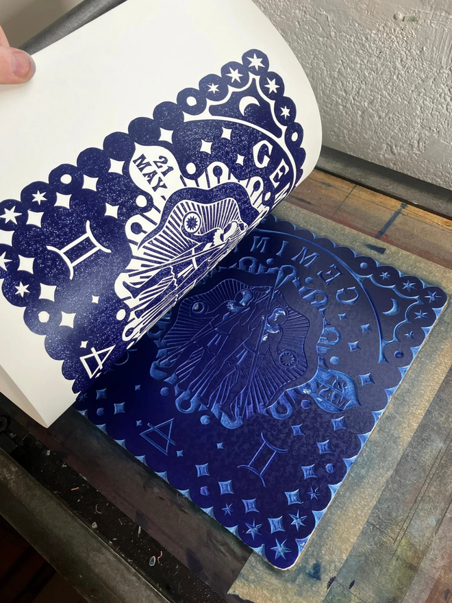 gemini zodiac linocut. twins and zodiac symbols linocut and printed on a blue background.