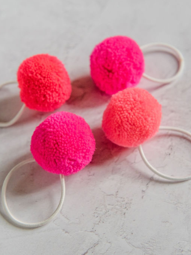 pom pom hair ties (set of four). four pom pom hair ties in shades of pink.