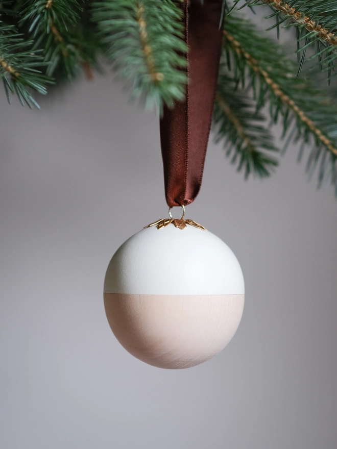 Wooden and white Christmas gift bauble with a removable lid, hanging from a Christmas tree with a space inside for a handwritten message, gift or surprise