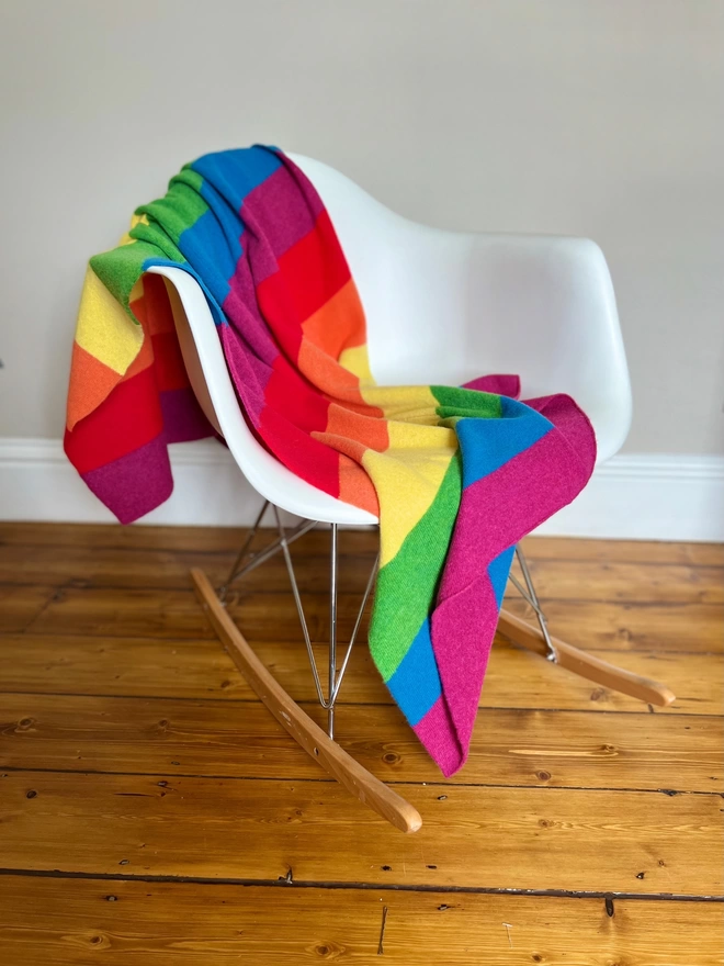 Knitted rainbow blanket shown draped over a chair