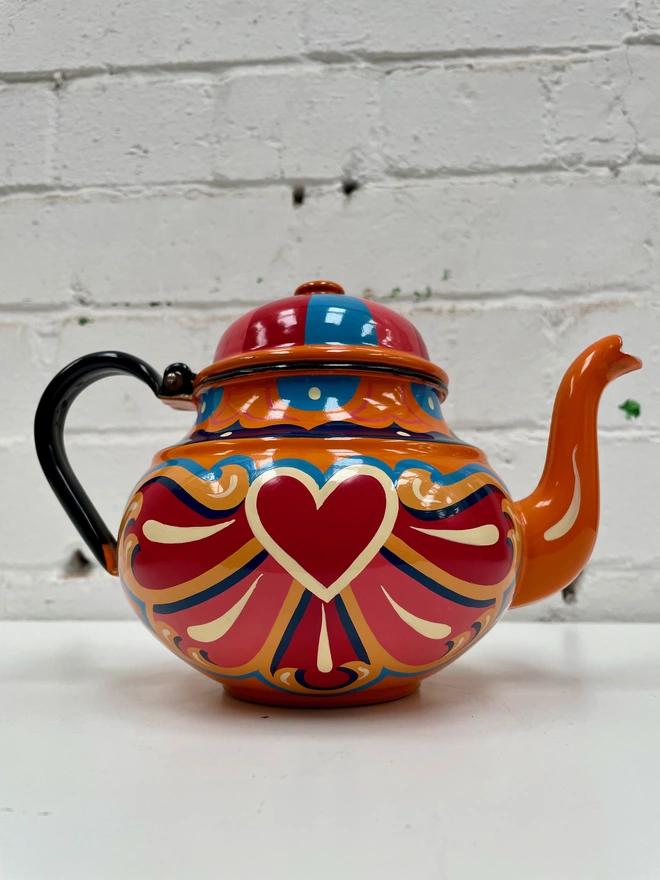 Orange vintage teapot with hinged lid, hand painted with a traditional fairground inspired design in pink, red, yellow and blue.