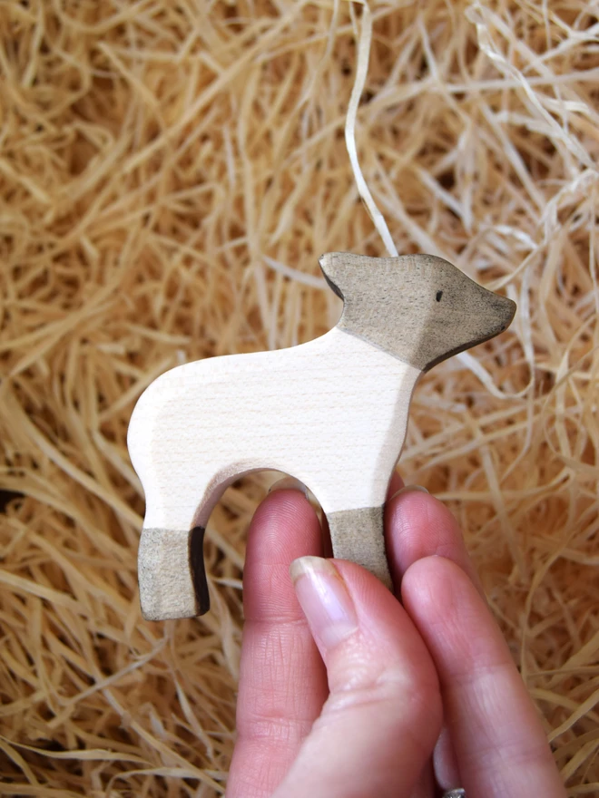 black and white lamb standing wooden toy held in hand above woodwool