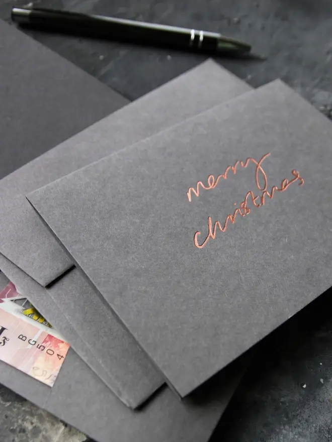 Hand foiled cash card or money wallet in a smoke grey colour in shiny bronze foil text which says ‘merry christmas’.