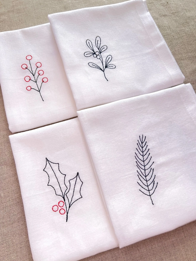 Set of four white cotton embroidered napkins with festive botanical designs, perfect for Christmas tables