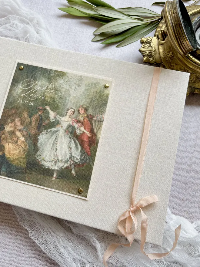 Luxury ivory linen guest book with a fabric printed image of dancers taken from an 18th century rococo work of art. A bow is added for a beautifully romantic finishing touch.