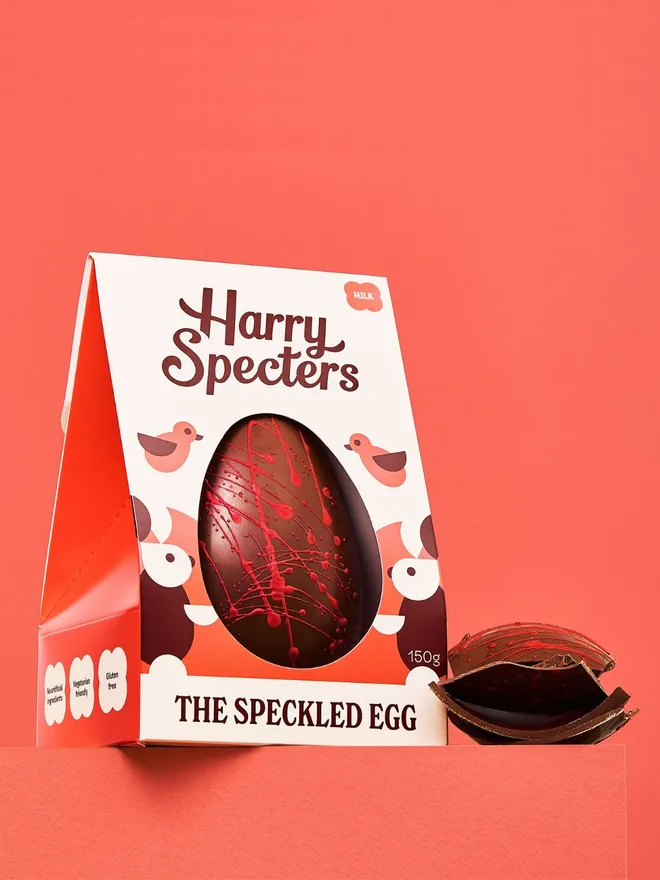 A milk chocolate Easter egg decorated with red speckles, next to a stack of milk chocolate Easter egg pieces