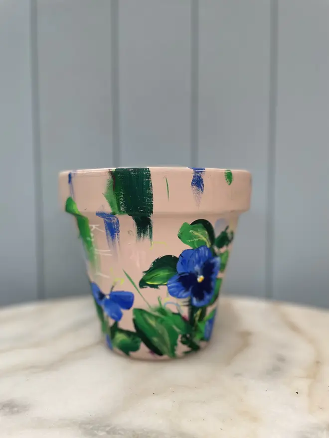 Unique hand-painted terracotta pot featuring blue pansy flowers on a natural stone background