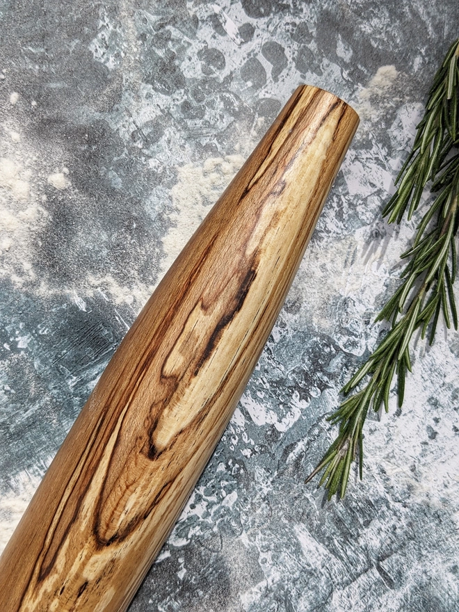 A highlight shot of a hand made rolling pin in Spalted Beech by Something From The Turnery, the picture is focussed on the right hand side of the rolling pin which boasts dramatic , all natural grain patterns.