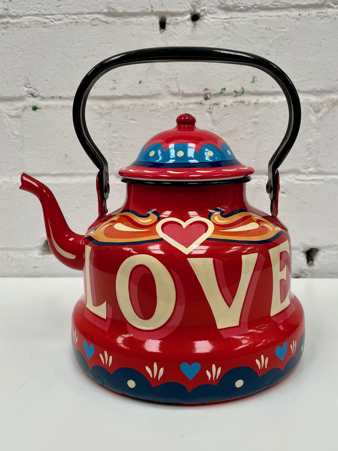 Red vintage enamel kettle, hand-painted with a fairground inspired design in orange, pink, yellow and blue. 'Love' is painted in large lettering across the centre.