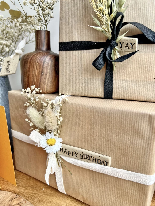 brown paper parcels tied with cotton ribbon, a selection of dried flowers and a handmade ceramic tag