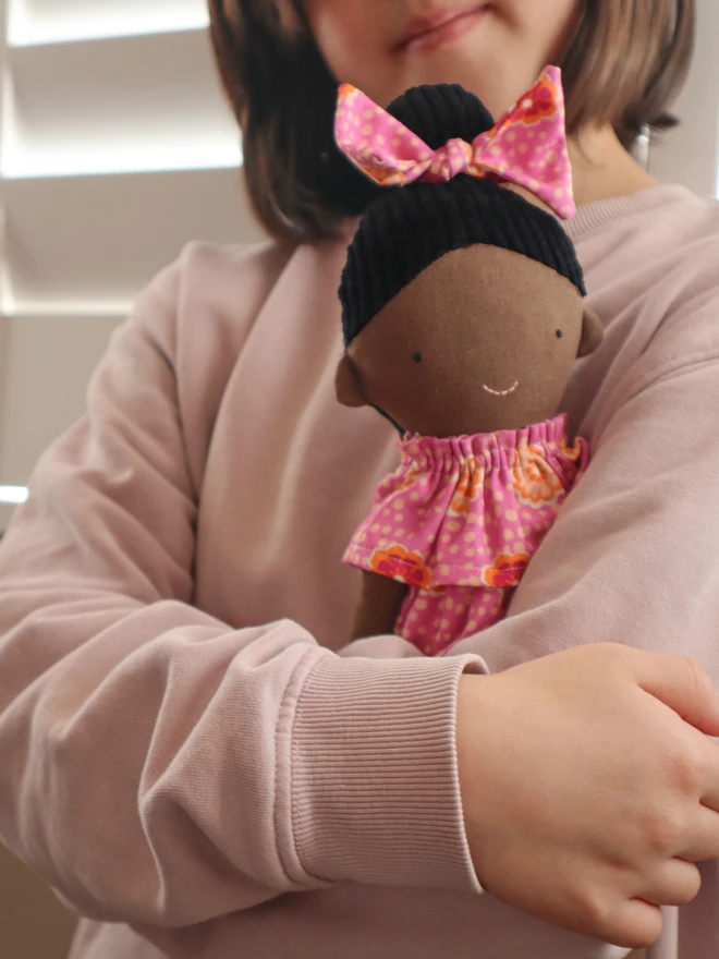 African-inspired handmade cloth doll with deep brown fabric skin, wearing a pink floral dress and matching bow