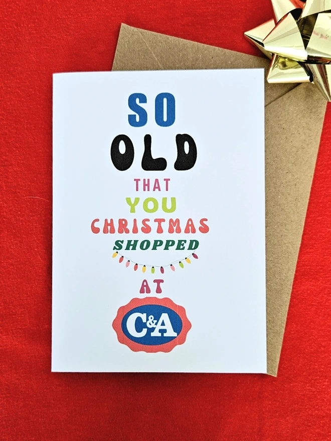 A photograph of the front of a humorous A6 greeting card illustrated using brightly coloured text and the retro shop logo. The text says so old you Christmas shopped at C&A with a string of colourful fairy lights.
