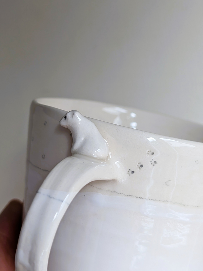 white cup with a close up of a pottery polar bear sitting on the handle with tiny paw prints on the cup