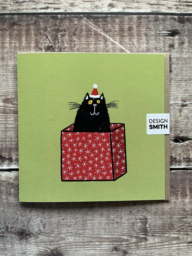 Card front featuring a cat in a Christmas box
